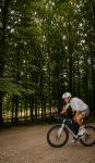 Robin Gemperle riding a gravel bike with a black Apidura frame pack along a forest track, trees blurred with motion behind him.